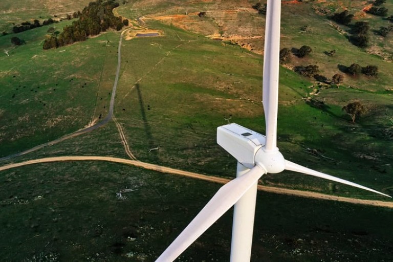 Wind turbine, wind farm in green field with dirt road, renewable energy in Australia